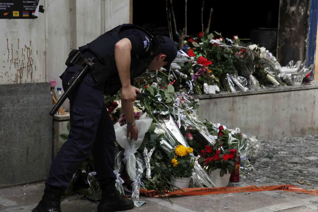 Für Blinde: Unser Archivfoto von Eurokinissi entstand 2010 vor der Marfin-Bank in Athen. Es zeigt einen Polizisten, der Blumen vor dem Gebäude der Bank niederlegt.