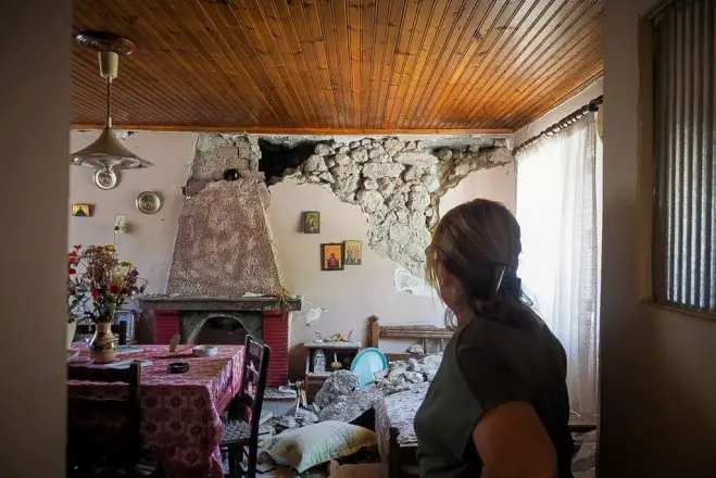 Unser Foto (© Eurokinissi) entstand am Sonntag (7.6.) auf Euböa. Es zeigt eine Frau vor der beschädigten Wand ihres Hauses. Teile des Putzes und Mauersteine waren auf ihr Bett gestürzt.
