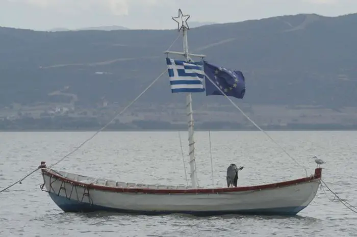 Auf unserem Foto ist ein Kaiki (© Eurokinissi) mit einer griechischen und europäischen Fahne zu sehen. Trotz der Bemühungen der EU, die Boote aus dem Verkehr zu ziehen, hisste der Bootsfahrer auch eine EU-Fahne.