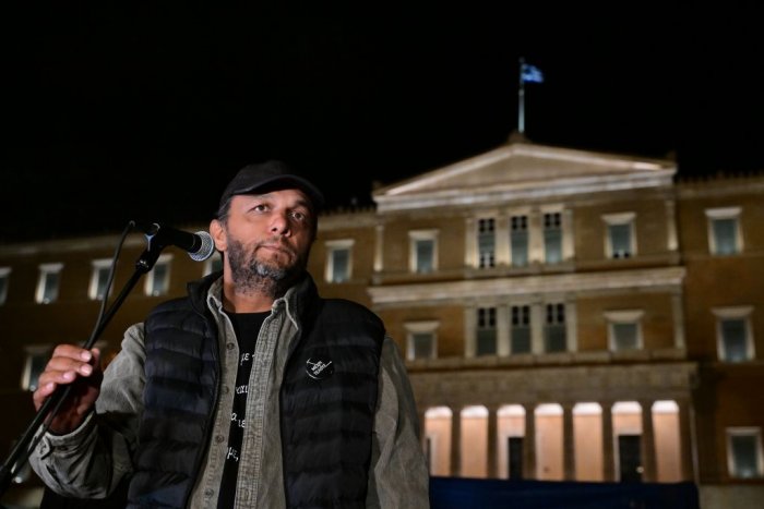 Unser Foto (© Eurokinissi) zeigt Panos Routsis während einer Rede vor dem Parlament. Auf der Kokarde an seiner Weste steht: „Bis zum Ende“ (Μέχρι Τέλους / Méchri Télous).