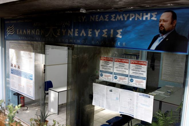 Unser Archivfoto (© Eurokinissi) entstand im Oktober 2016 nach einem Anschlag mit zwei Gaskartuschen auf das Parteibüro von Artémis Sórras in Nea Smyrni, einem Vorort von Athen. Rechts im Bild auf dem Transparent: der Parteigründer persönlich.