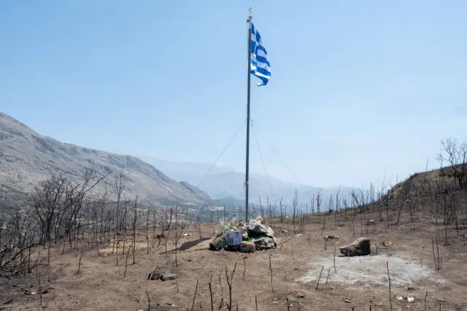 Unser Foto (© Eurokinissi) zeigt eine griechische Flagge in der verbrannten Landschaft südlich von Rethymnon, die an die beiden Feuerwehrleute Pantelis Diamantakis (25) und Manolis Stratidakis (58) erinnert, die während der Löscharbeiten ums Leben kamen.