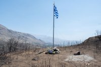 Unser Foto (© Eurokinissi) zeigt eine griechische Flagge in der verbrannten Landschaft südlich von Rethymnon, die an die beiden Feuerwehrleute Pantelis Diamantakis (25) und Manolis Stratidakis (58) erinnert, die während der Löscharbeiten ums Leben kamen.