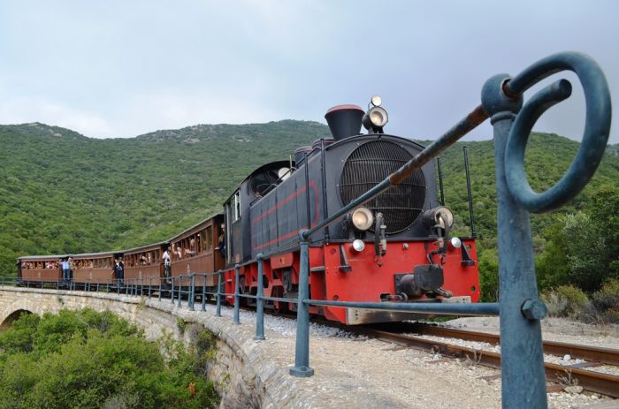 Das Foto (© Griechenland Zeitung / Jan Hübel) zeigt die Schmalspurbahn, die von Ano Lechonia bei Volos ins Pilion-Gebirge fährt. Endstation ist der Ort Milies, der viele Sehenswürdigkeiten zu bieten hat. Auch schon auf dem Weg dorthin kann man in der Kleinbahn einiges erleben.