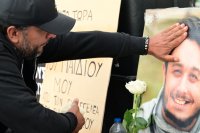 Unser Foto (© Eurokinissi) zeigt Panos Routsis am Syntagma-Platz in Athen. Vor ihm ein Bild seines Sohnes, Denis, der 2023 bei einem Bahnunglück ums Leben kam.